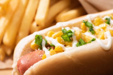 Patates kızartmasının yanında mısır, yeşil soğan ve mayonez ile nefis sosisli sandviçi yakından izleyin.
