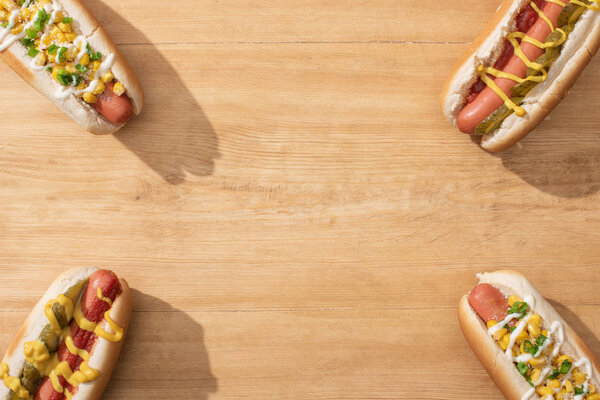 top view of delicious hot dogs with corn, green onion and pickles on wooden table