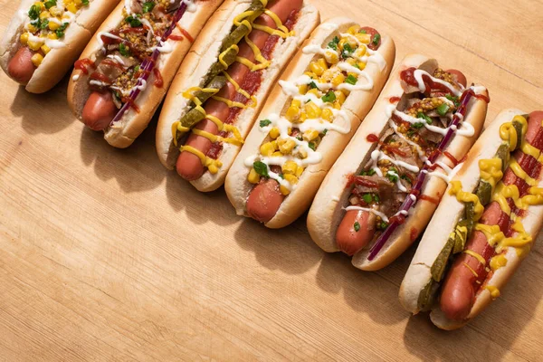 various delicious hot dogs with vegetables and sauces on wooden table