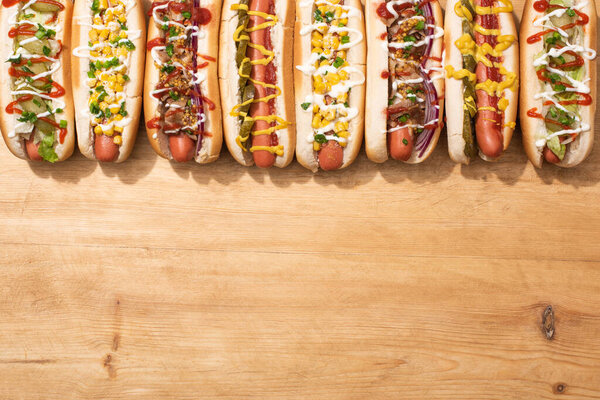 top view of various delicious hot dogs with vegetables and sauces on wooden table