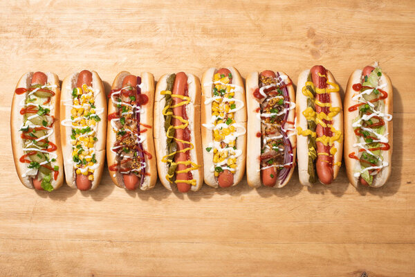 top view of various delicious hot dogs with vegetables and sauces on wooden table