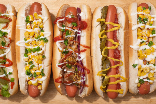 top view of various delicious hot dogs with vegetables and sauces on wooden table