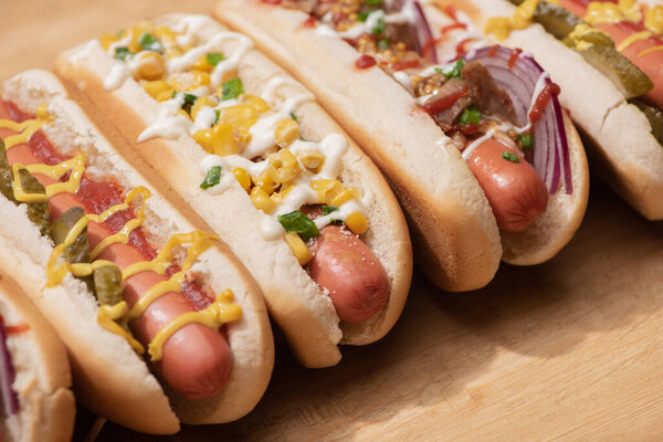 различные вкусные хот-доги с овощами и соусами на деревянном столе
