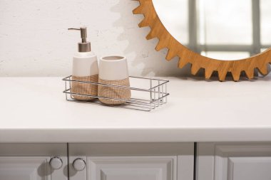 Dispenser liquid soap, toothbrush holder on shelf near round mirror on wall in bathroom, zero waste concept clipart