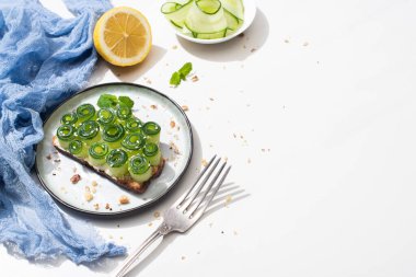 Susamlı taze salatalıklı tost, çatalın yanında nane yaprakları ve beyaz arka planda limon.