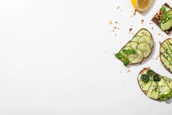 top view of fresh cucumber toasts with seeds, mint and basil leaves and lemon on white background