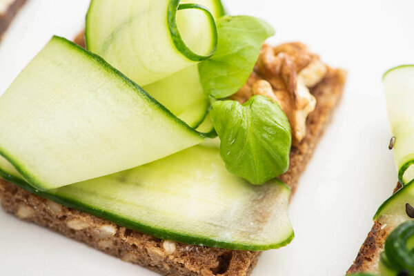 close up view of fresh cucumber toast with walnut and basil leaves isolated on white
