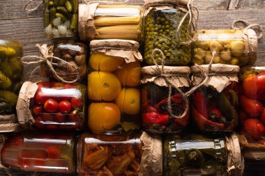 top view of delicious pickles in jars on wooden table clipart