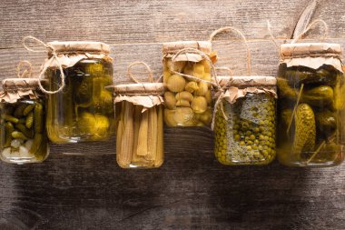 top view of green tasty homemade pickles in jars on wooden rustic table clipart