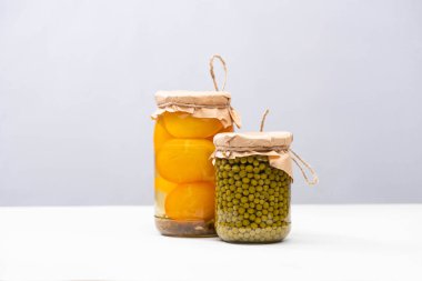 homemade delicious pickled yellow tomatoes and green peas in jars isolated on grey clipart