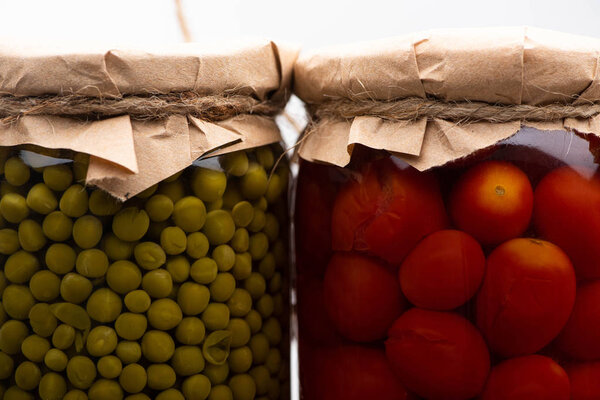 close up view of homemade tasty canned tomatoes and green peas in jars