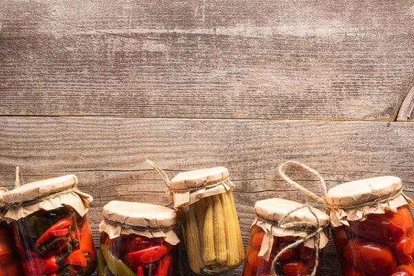 top view of homemade tasty pickles in jars on wooden table with copy space