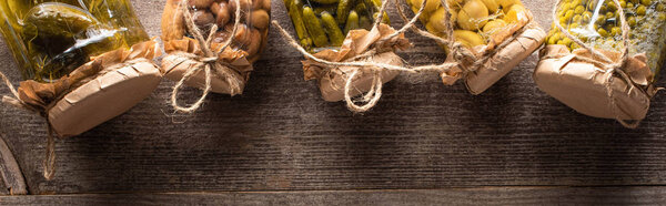 top view of homemade tasty pickles in jars on wooden table with copy space, panoramic shot