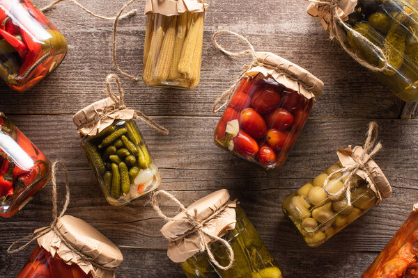 top view of fresh homemade tasty pickles in jars on wooden table