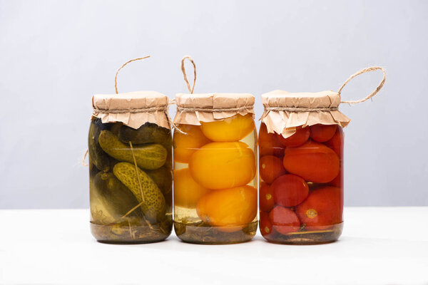 homemade delicious pickled tomatoes and cucumbers in jars isolated on grey