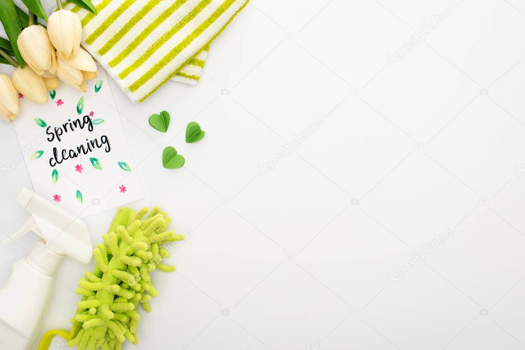 top view of spring tulips and green cleaning supplies near spring cleaning card on white background