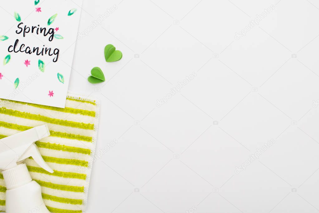 top view of green cleaning supplies with hearts near spring cleaning card on white background