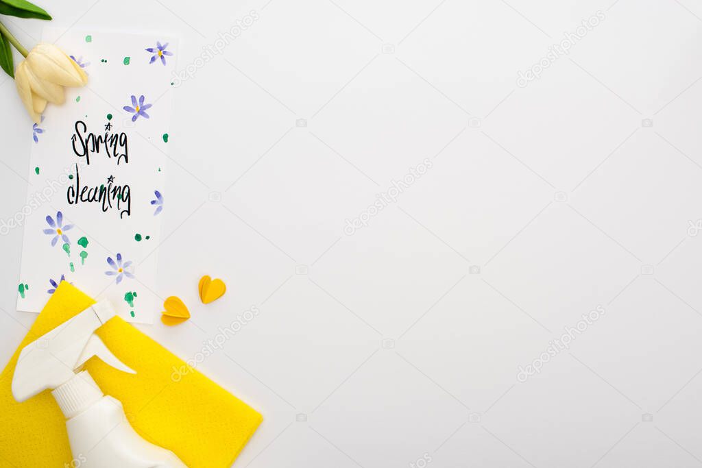 top view of spring tulips and yellow cleaning supplies near spring cleaning card on white background