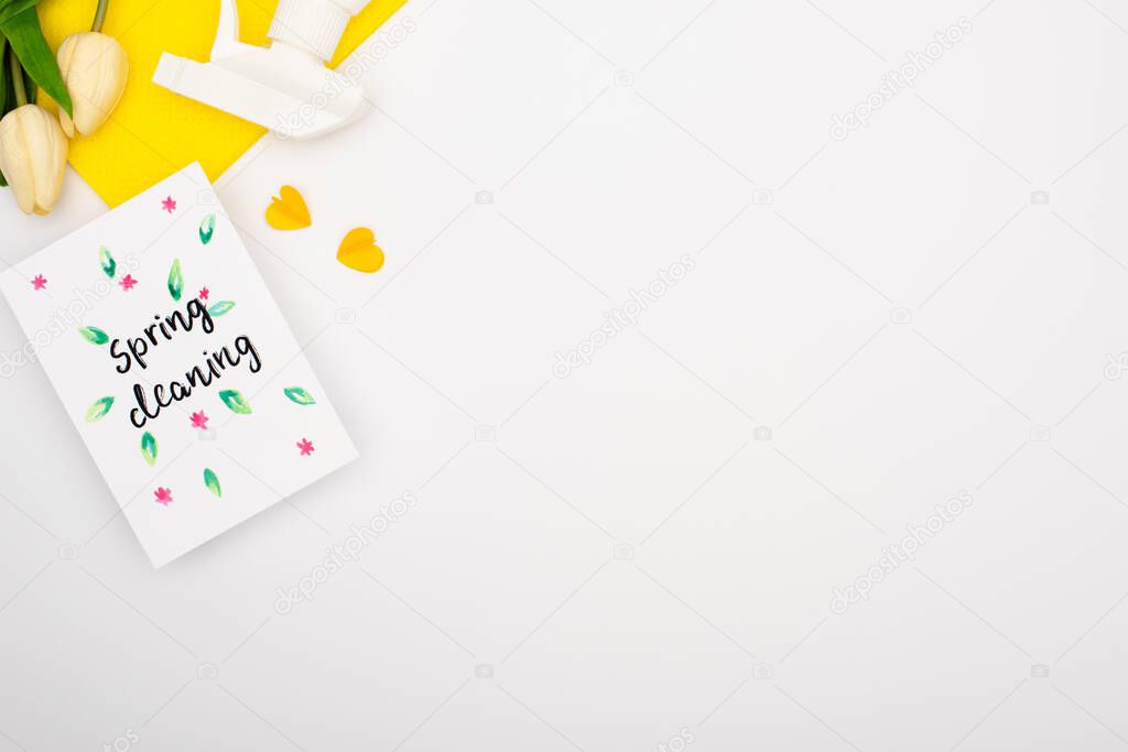 top view of spring tulips and yellow cleaning supplies near spring cleaning card on white background