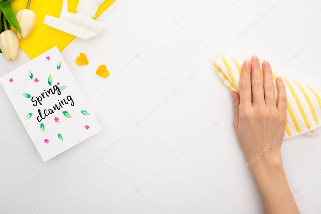 cropped view of woman holding rag near spring tulips, yellow cleaning supplies, spring cleaning card on white background