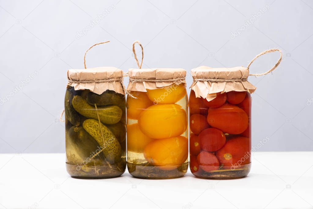 homemade delicious pickled tomatoes and cucumbers in jars isolated on grey