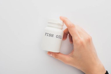 Cropped view of woman holding container with fish oil lettering on white background clipart