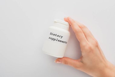 Beyaz arka planda besin takviyeleri olan bir kadın konteynırını elinde tutarken çekilmiş görüntüsü