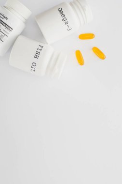 Beyaz arka planda sarı kapsüllerin yanında balık yağı ve omega-3 harfli konteynırların üst görüntüsü