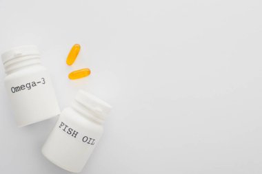 Top view of containers with fish oil and omega-3 lettering near capsules on white background clipart