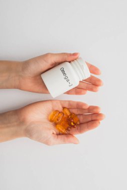 Beyaz kapsüllü ve omega-3 harfli konteynırları tutan kadın görüntüsü. 