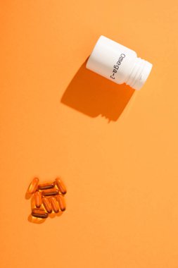 Turuncu zemin üzerinde omega-3 harfleri ve kapsülleri olan konteynırın üst görünümü