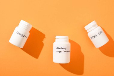 Omega-3 'lü konteynırların üst görüntüsü, turuncu arka planda yazılı balık yağı ve diyet takviyeleri