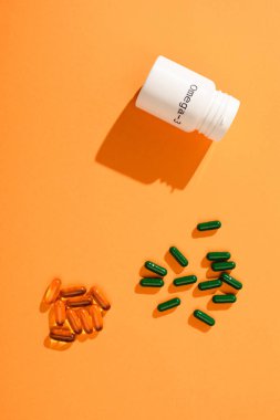 Top view of container with omega-3 lettering and capsules on orange  clipart