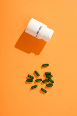 Omega-3 harfli konteynır ve turuncu arka planda yeşil kapsüllerin üst görünümü