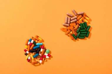 Top view of colorful pills and capsules on orange background clipart