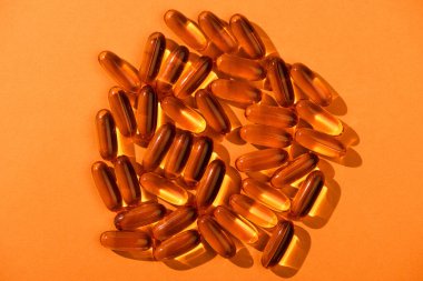Top view of brown fish oil capsules on orange background clipart