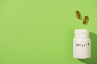 Yeşil kapsüllerin yanında omega-3 harfleri olan konteynırın üst görünümü