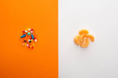Top view of colorful pills and mandarin on white and orange  clipart