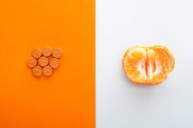 Beyaz ve turuncu arka planda hapların ve mandalinanın üst görüntüsü