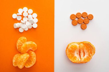 Top view of dietary supplements and mandarin on white and orange background clipart