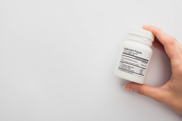 Cropped view of woman holding container with dietary supplements on white 