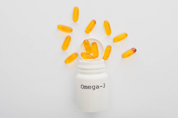 Верхний вид открытого контейнера с омега-3 желтыми капсулами на белом фоне

