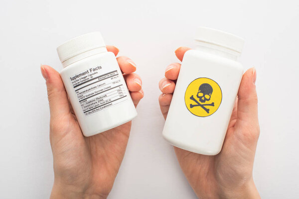 Cropped view of woman holding containers with dietary supplements and dangerous poison on white 