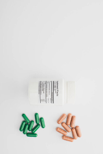 Top view of container with brown and green capsules on white background 