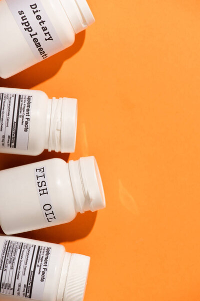 Вид сверху контейнеров с рыбьим жиром и диетическими продуктами на оранжевом фоне
