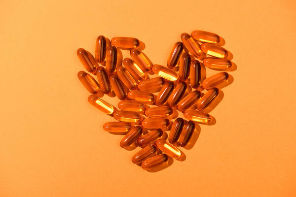 Top view of decorative heart from fish oil capsules on orange background
