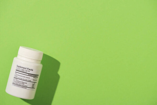 Top view of white container with dietary supplements on green background