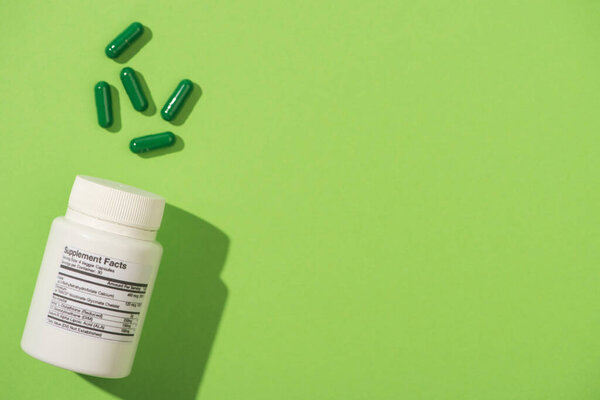 Top view of white container near capsules on green background