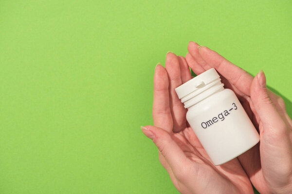 Обрезанный вид женщины, держащей контейнер с надписью омега-3 на зеленом фоне
