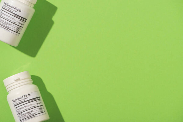 Top view of containers with dietary supplements on green 